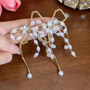 Detailed view of elegant gold bow earrings with pearls and zircons on wooden background