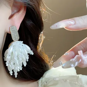 Close-up detail of elegant gold-tone rhinestone and white pearl tassel earrings on ear.