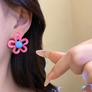 Close-up detail of a pink resin flower earring with a blue center on a model