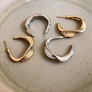 Minimalist twisted C-shaped hoop earrings with wrinkled texture in gold and silver