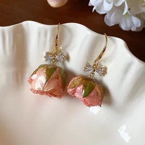 Close-up of preserved rose bud earrings with zircon bow detail on white ceramic