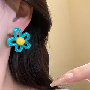Detailed macro view of a blue and yellow resin flower stud earring worn on a person's ear