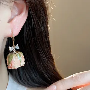 Close-up detail of a delicate preserved pink rose earring featuring a zircon bow accent