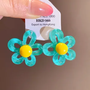 Close-up of teal resin flower stud earrings with yellow centers on a display card