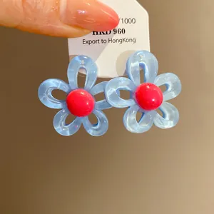 Detail of light blue resin flower stud earrings with vibrant red centers on a card.