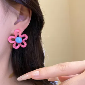 Macro detail of sweet pink resin flower stud earring worn on ear with blue center