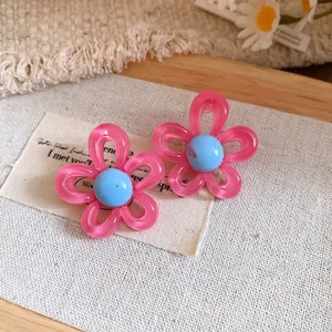 Close-up of pink resin flower stud earrings with blue center on a fabric background