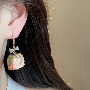 Macro detail of elegant zircon bowknot ear hook with a realistic pink eternal rose bud.