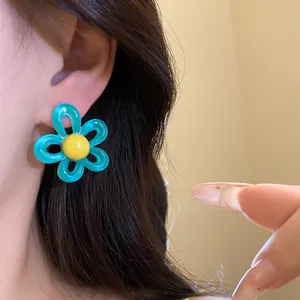 Close-up of a sweet blue resin flower earring with a bright yellow center on ear