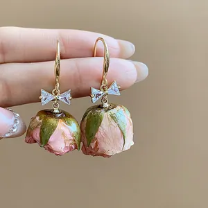 Close-up of elegant zircon bow earrings with delicate pink preserved rose buds.