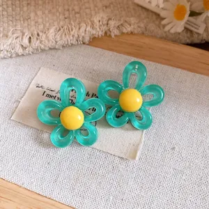 Detail showing teal resin flower earrings with yellow centers on rustic fabric background