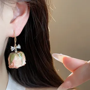 Detail shot of a zircon bow and real preserved rose bud ear hook earring on model.