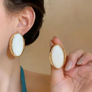 Vintage oversized oval resin stud earrings with gold frame, shown on ear and held.