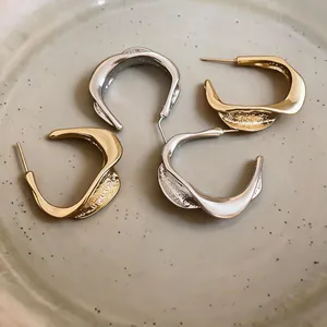 Detail shot of elegant gold and silver twisted C-shaped hoop earrings with crinkled texture