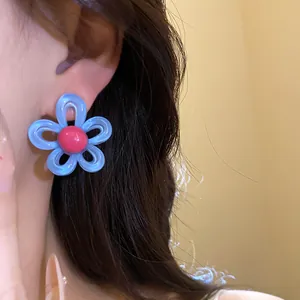Detailed close-up showing a blue and red resin flower stud earring worn on model's ear
