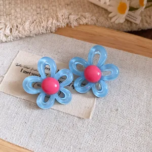 Close-up view of blue resin flower stud earrings with pink center on canvas