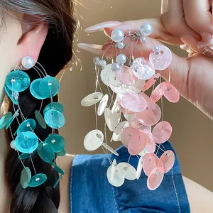 Detalle de pendientes de borla con discos de concha, perlas y aguja de plata.