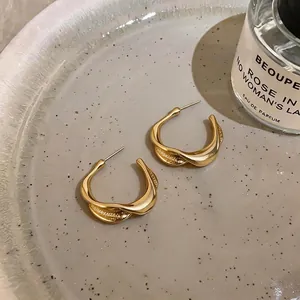 Close-up of minimalist gold pleated twisted C-shape hoop earrings on a ceramic plate