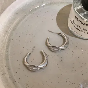 Detail view of silver twisted C-shaped stud earrings with micro-inlaid stones on ceramic plate.