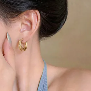 Close-up detail of gold pleated twisted C-shaped hoop earrings worn by a female model