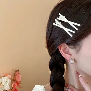 Elegant minimalist cream X-shaped hair clips paired with pearl earrings on model