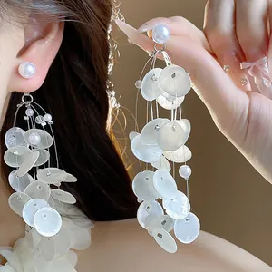 Detalle en primer plano de elegantes pendientes de borla de concha blanca y perla para playa