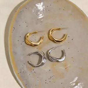 Detailed macro view of twisted C-shaped earrings in polished gold and silver finishes