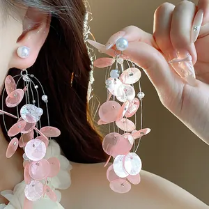 Primer plano de pendientes de borla de nácar rosa con perlas y delicados hilos metálicos