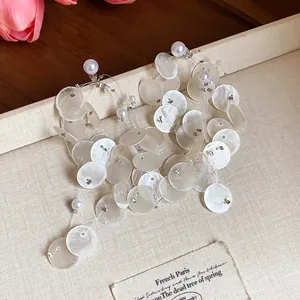 Primer plano de elegantes pendientes de flecos de concha con perlas en fondo beige