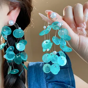 Primer plano detallado de pendientes de borla de concha turquesa con perlas en modelo