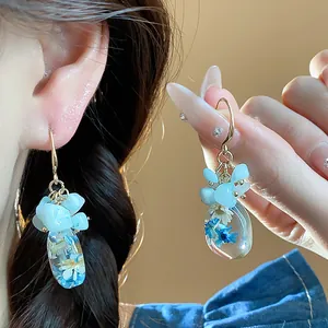 Close-up view of ethnic blue floral resin earrings with natural stones worn by model
