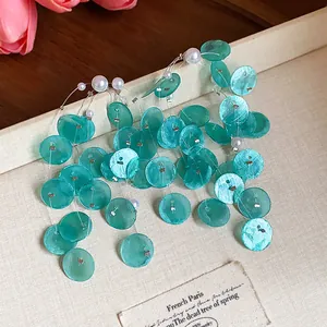 Primer plano de elegantes pendientes de borla con discos de concha verde y perlas blancas
