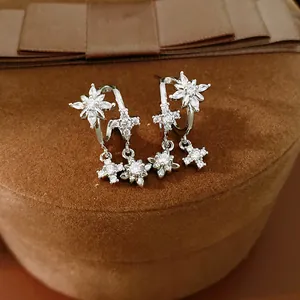 Dettaglio di orecchini in argento con stelle e croci in zircone su scatola di velluto marrone.