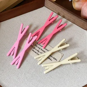 Detailed macro view of minimalist X-shaped duckbill hair clips in pink and cream tones