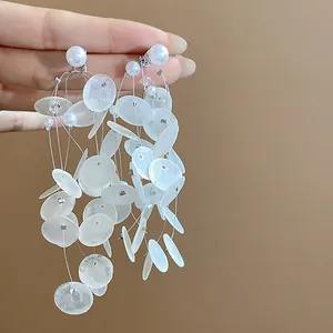 Primer plano de pendientes de borla con discos de concha y perlas con aguja de plata