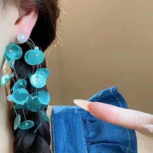 Primer plano de elegantes pendientes de borla con discos de concha azul y perlas.