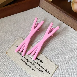 Pair of trendy minimalist matte pink Y-shaped duckbill hair clips on fabric backdrop