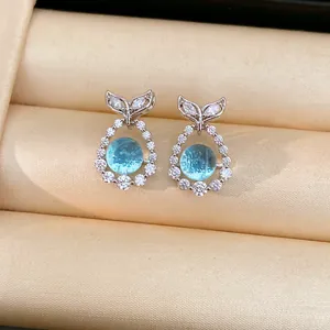 Detail view of silver fish tail stud earrings featuring sparkling zircon and blue center stones