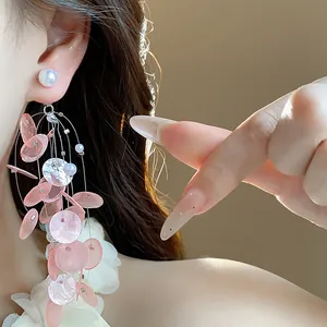 Detalle macro de elegantes pendientes largos de borla de concha rosa con perlas al oído