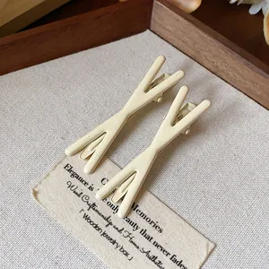 Detail view of two minimalist cream-colored Y-shaped alligator hair clips on fabric