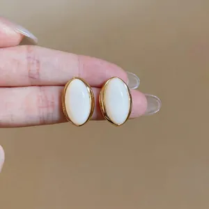 Close-up view of vintage style oval white resin stud earrings with gold-toned bezels