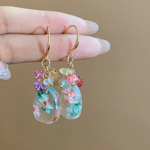 Close-up of elegant resin drop earrings featuring dried flowers and vibrant natural stones