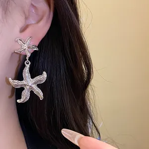 Close-up detail of silver starfish pendant earrings with pleated metallic texture