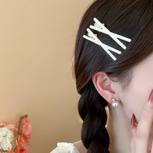 Detail shot of two cream-white X-shaped hair clips styled on a braided hairstyle