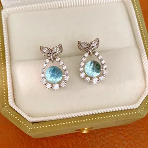Close-up of elegant silver fishtail earrings featuring light blue round zircon in a box