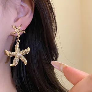 Close-up of elegant gold textured starfish drop earrings worn on ear.