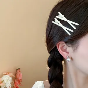Side view detail of a model wearing minimalist cream-colored cross-shaped hair clips