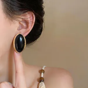 Vintage-style oval black resin stud earring with gold-tone border shown on a model's ear