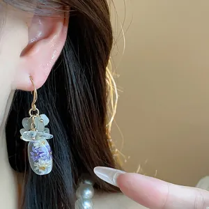 Detail shot of handmade resin earrings featuring real purple dried flowers and stones.
