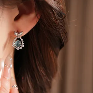 Close-up of elegant silver fishtail earrings with light blue gemstone and zircons